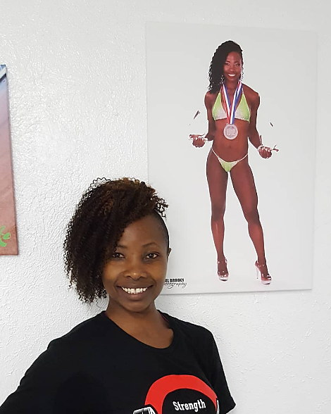 Betty smiling in a Strength tee, beside a framed photograph of herself competing