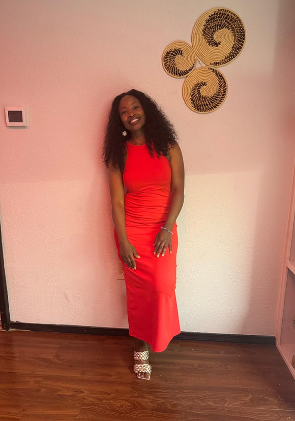 Standing against a pale wall hung with woven sisal baskets, in a red dress