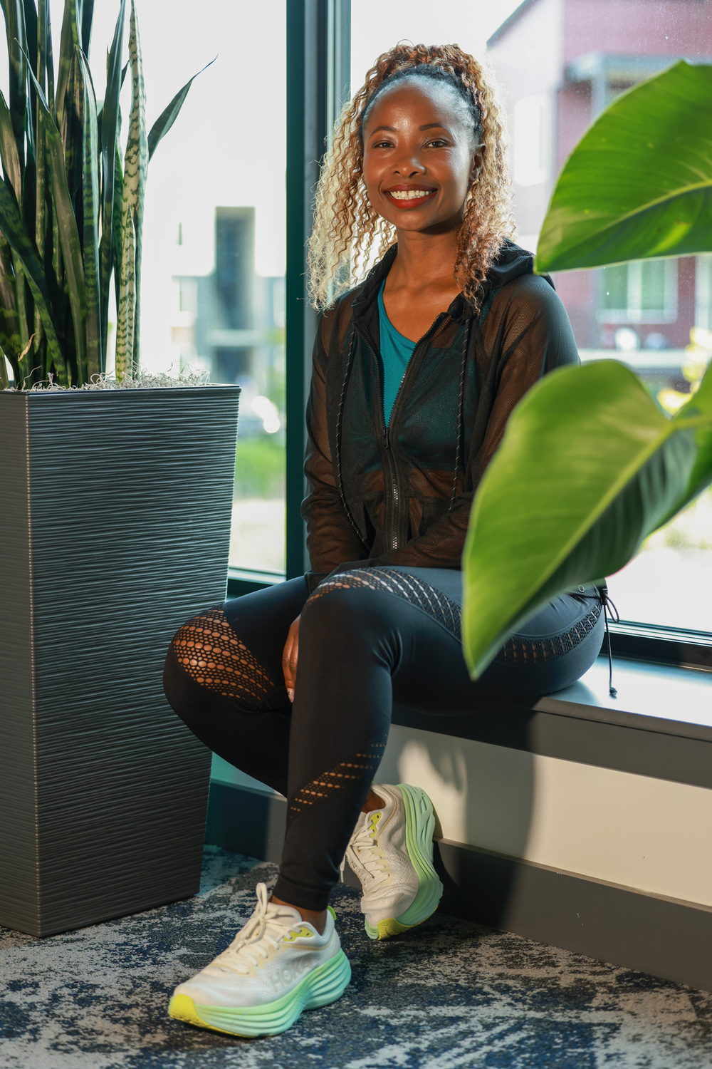 Betty sitting on a windowsill in a black hoodie and running shoes, smiling