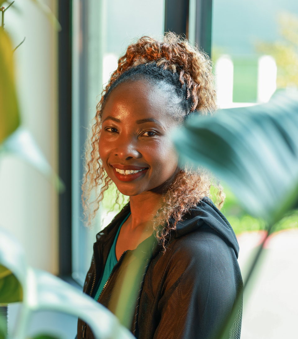 Betty laughing beside a window, between the leaves of a houseplant