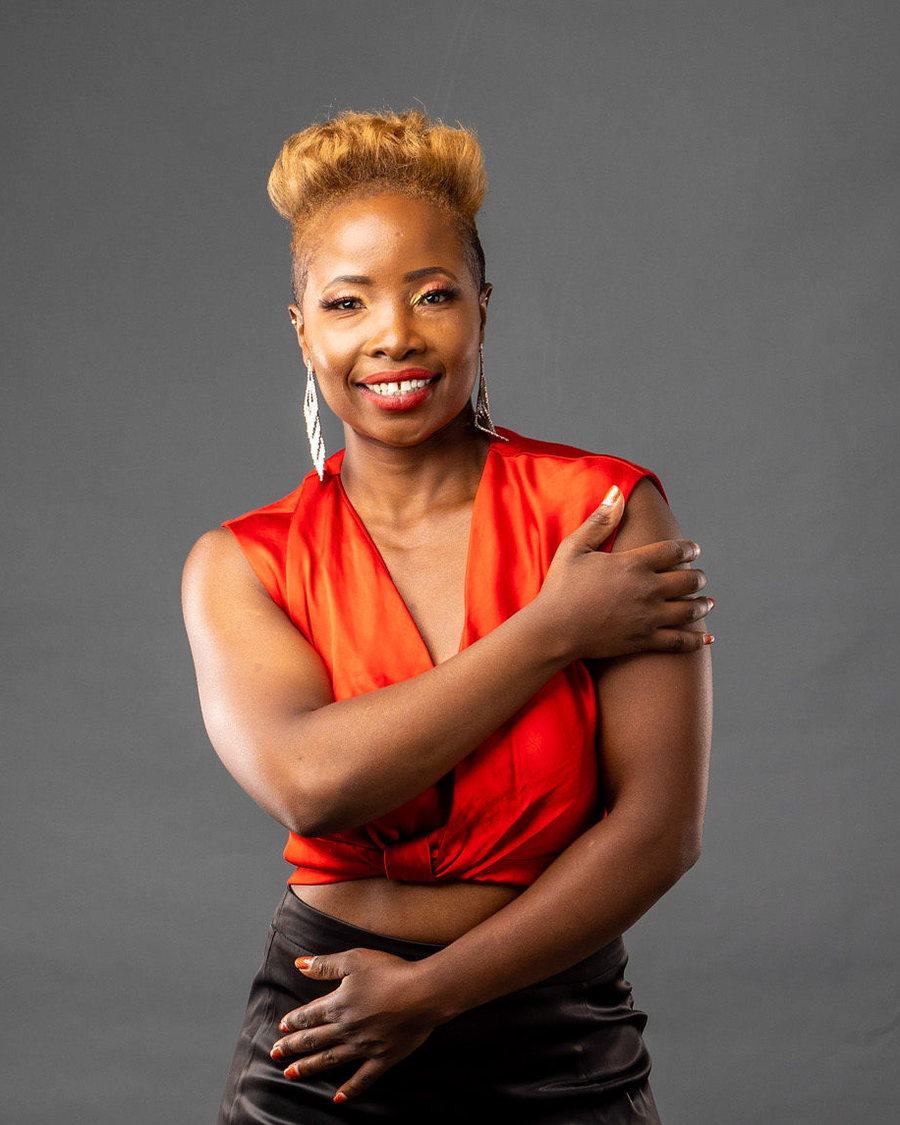 Betty in a red satin top, arms folded, smiling at the camera against a grey studio backdrop