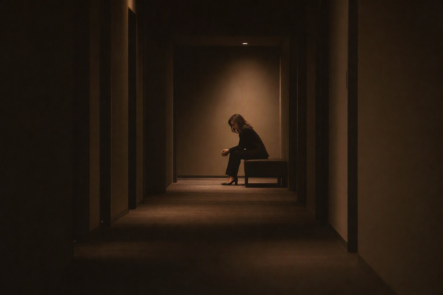 A woman sitting alone under a single light in a dark corridor, composing herself before going on.