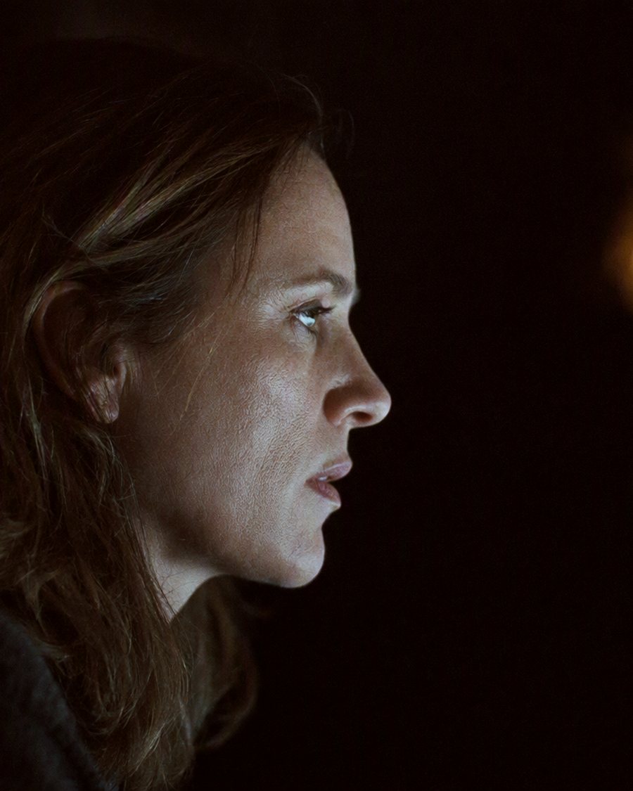 A producer in profile at a darkened desk, her face lit by the glow of screens out of frame.
