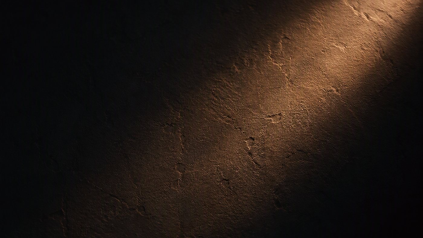 A dark plaster surface raked by a single shaft of warm light.